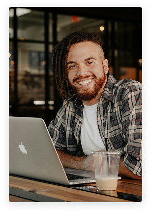 Man in a coffee shop smiling while on his laptop